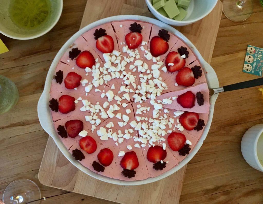Ein rosa-farbener Erdbeer-Kuchen von oben aufgenommen, in einer runden Form. Unter einem Kuchenstück befindet sich ein Tortenheber – bereit, gegriffen zu werden.