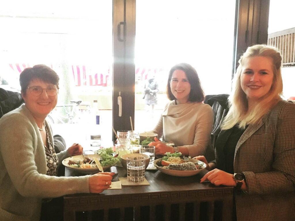 Anna Brandes und zwei Frauen sitzen an einem reich gedeckten Tisch im Restaurant.