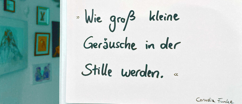 Ein per Hand geschriebenes Blatt an der Wand mit einem Zitat von Cornelia Funke. Es lautet „Wie groß kleine Geräusche in der Stille werden.“