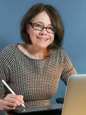 Anja Weiss Profilbild von Anja Weiss. Sie trägt ein kariertes Kleid und sitzt mit iPad und passendem Stift an einem Tisch und blickt lächelnd in die Kamera.
